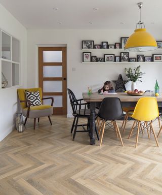 herringbone style wooden effect LVT flooring in dining room with child sat at table colouring