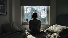 Rear view of a mature woman sitting on a bed and looking out of her window