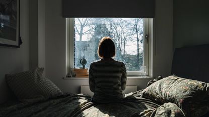 Rear view of a mature woman sitting on a bed and looking out of her window