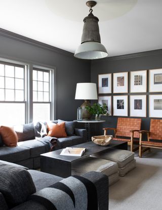 A living room in deep grey tones with orange chairs and pillows
