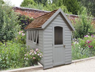 gray wooden shed in garden with windows and tiled roof