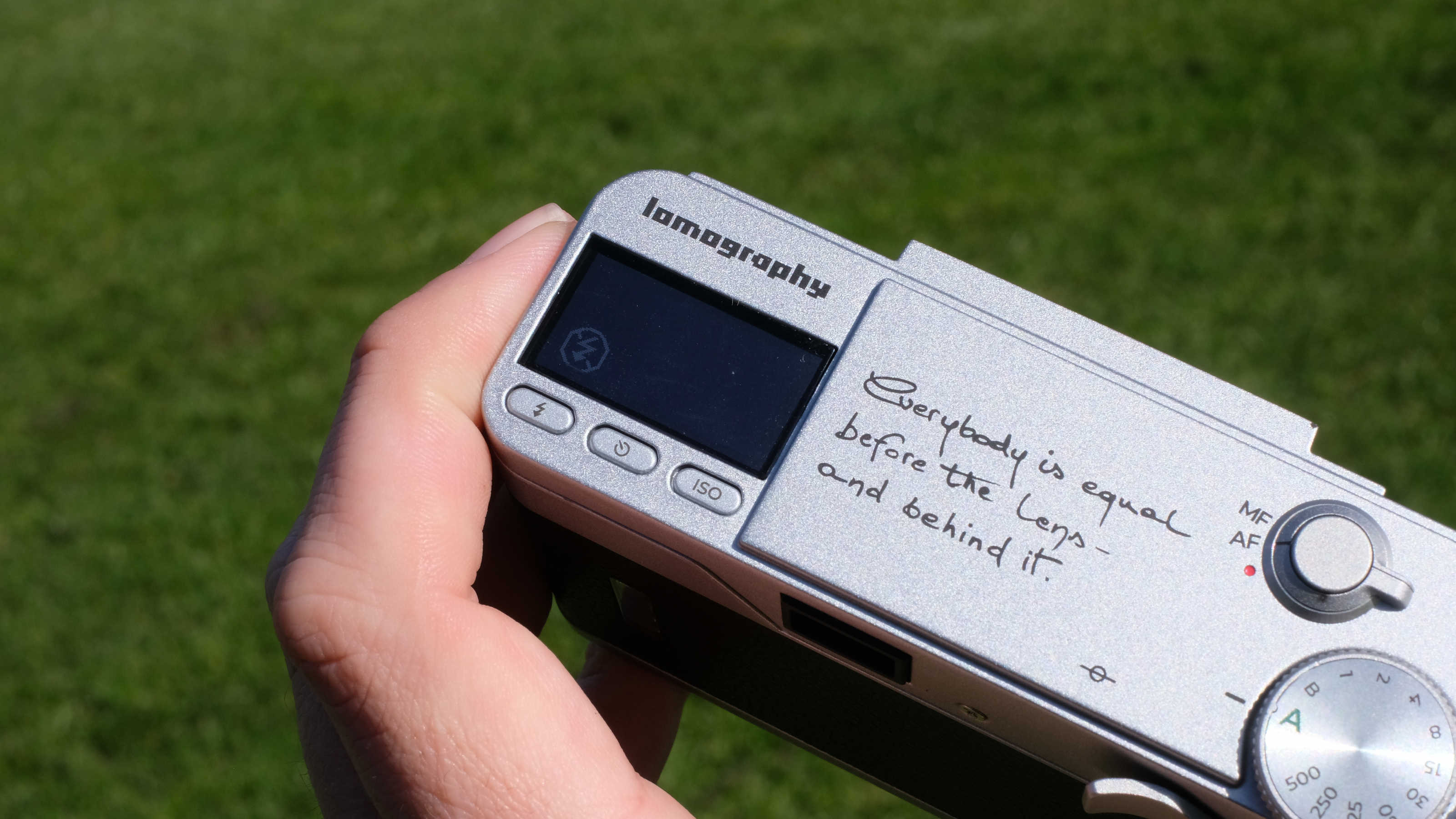 Photograph of the Lomography Lomo MC-A, with grass visible in background, showing detail of top plate and LCD screen