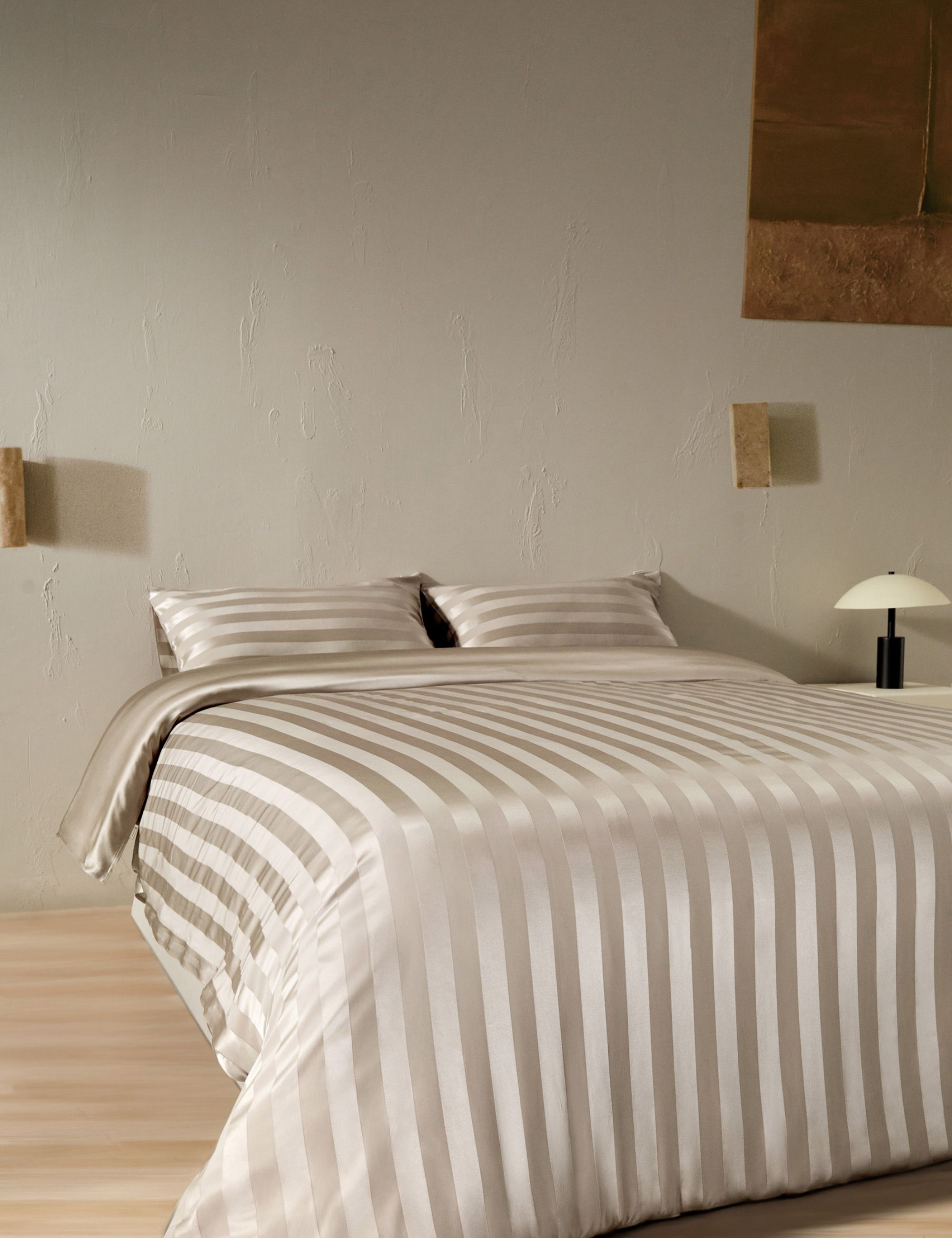 Striped silk bedding set pictured in a neutral minimalist bedroom with art