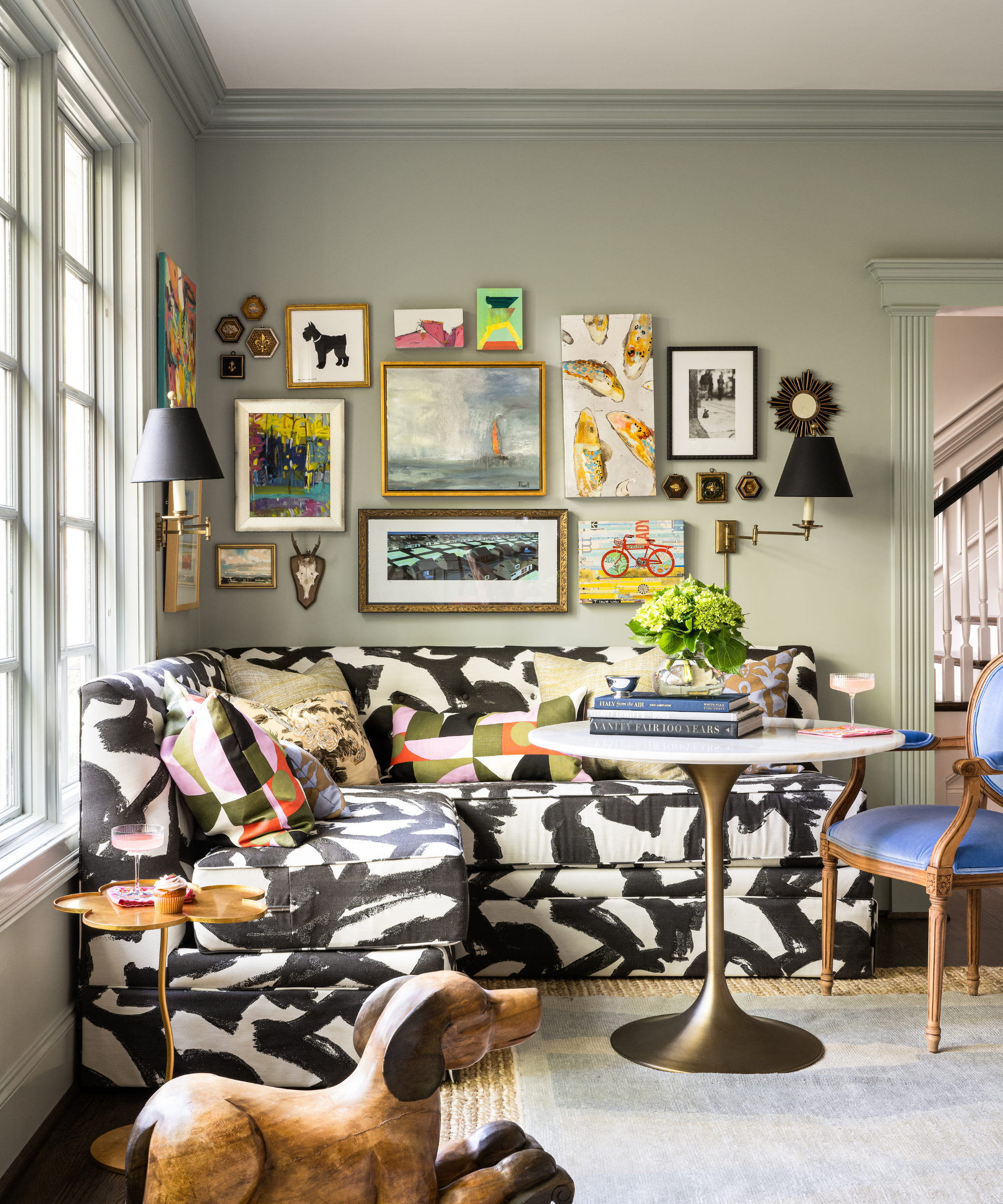 a corner seating area with a black and white abstract couch, a tulip table, and lots of art hung in the corner