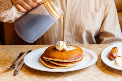 Man pouring maple syrup over pancakes in the diner .