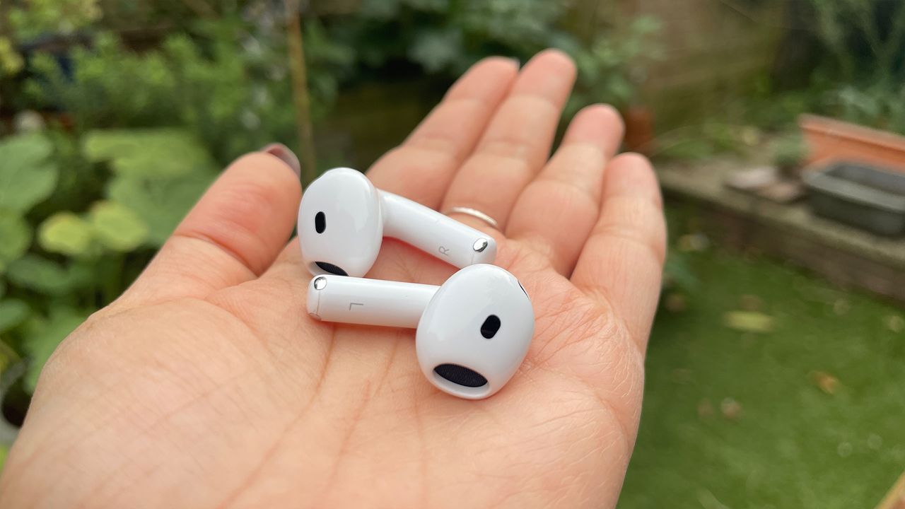 The Apple AirPods 4 with ANC earbuds held in an open hand in a garden.