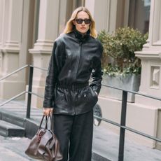 New York Fashion Week Attendee wears a peplum leather jacket with black trousers and a brown bag.