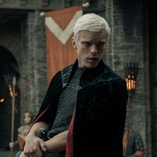 finn bennett as prince aerion targaryen riding on horseback through a medieval town in a still from a knight of seven kingdoms