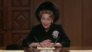 Faye Dunaway as Joan Crawford, sitting at a table with a fancy hat on in Mommie Dearest.