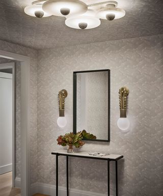 Lightly patterned wallpaper in entryway with large mirror and artistic lighting
