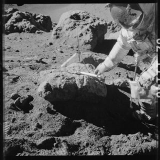 apollo astronaut leaning over rock with a gnomon placed on top