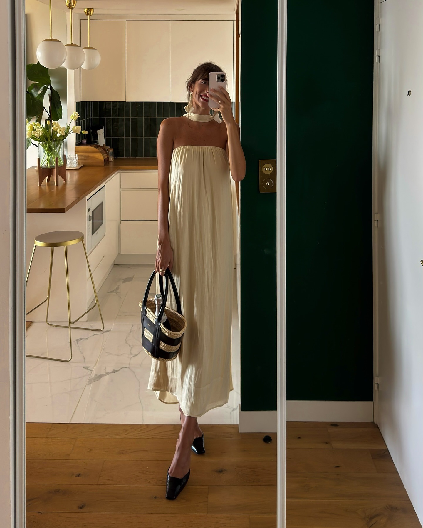 French influencer @juliesfi takes a mirror selfie wearing a white strapless dress with a wicker back and black closed-toe heeled mules.