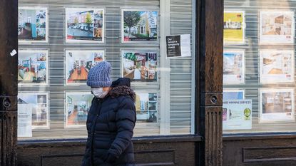 A pedestrian with a face mask passes a closed estate agent ©