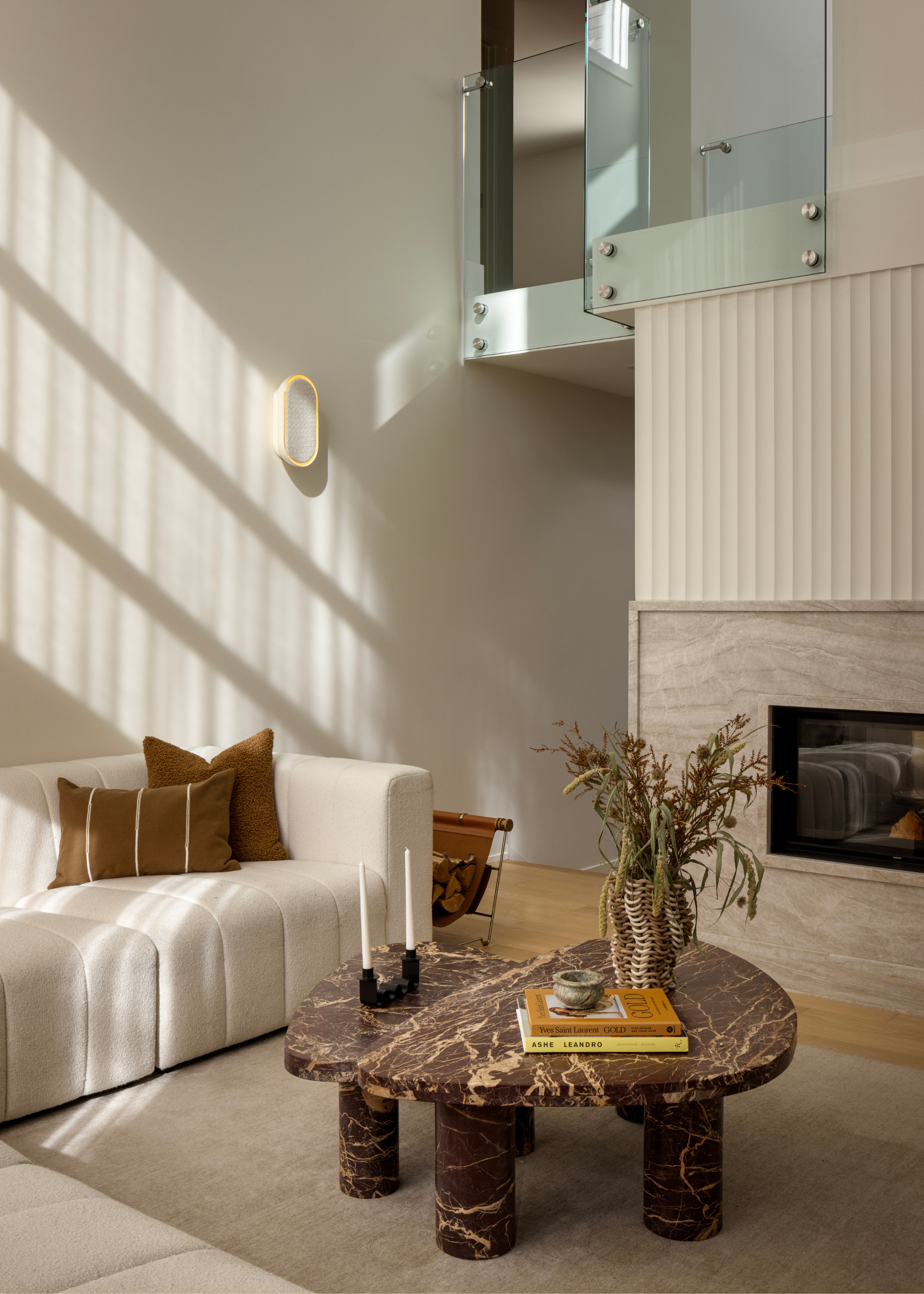 A bright living room with a white sofa, a marble coffee table, a log rack, and coffee table books