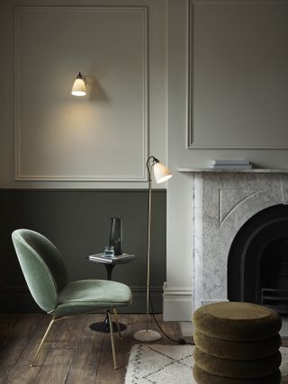 two tone green living room with marble fire surround, velvet chair and footstool, wall light, floor light, side table, rug