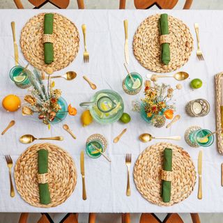 Overhead shot of white table with rattan placemats, green napkins, gold cutlery and glasses