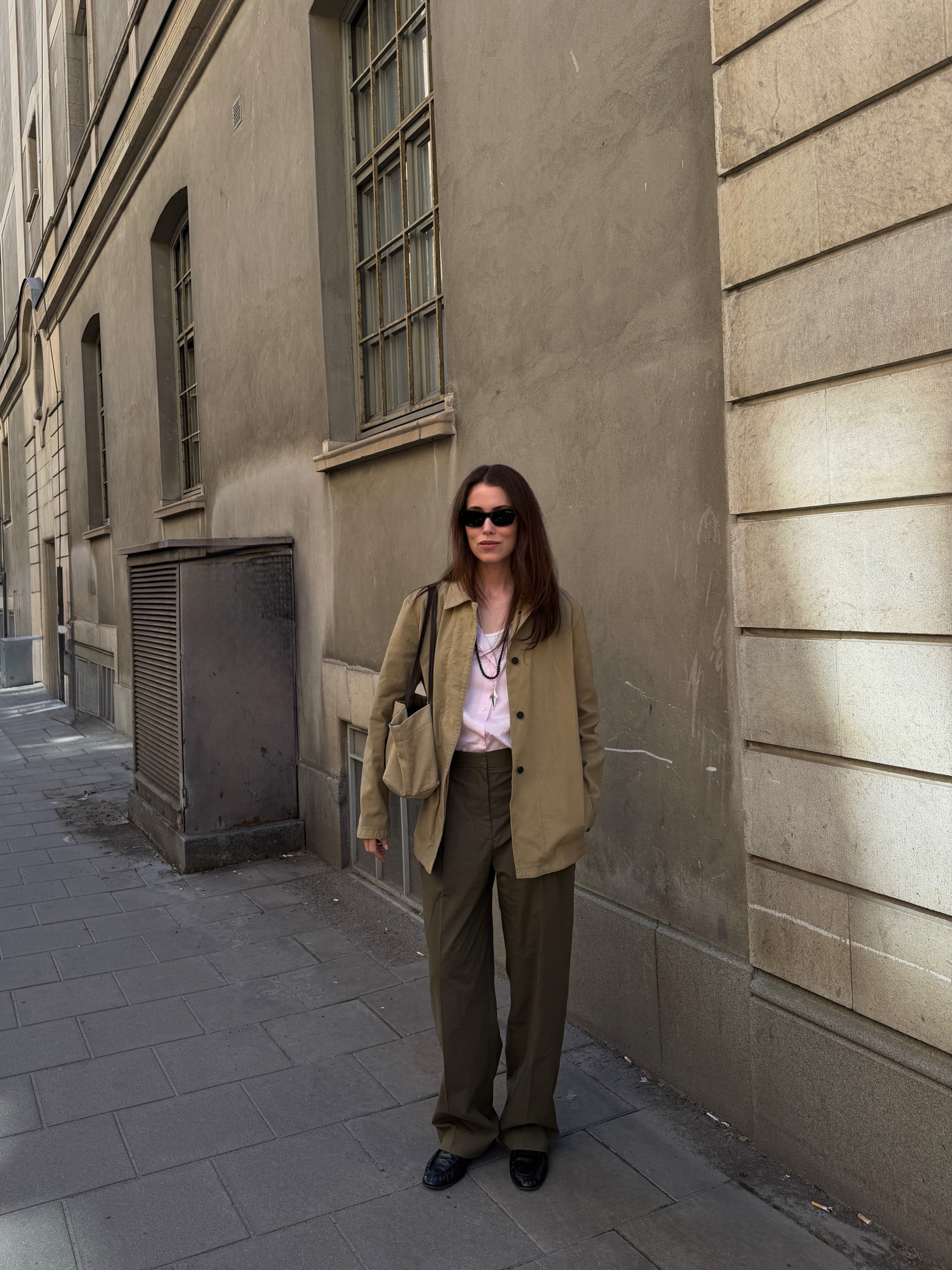 An image of an influencer in a beige canvas jacket, a pink linen shirt, brown trousers and loafers.