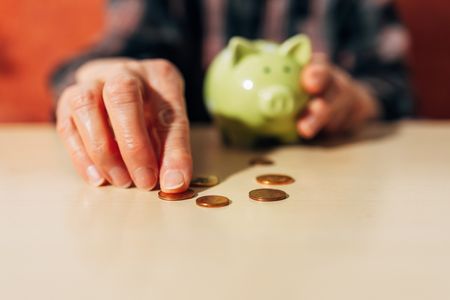 A close up of a senior man's hands as he counts pennies from his piggy bank.