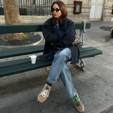 Influencer wears brown suede trainers and jeans whilst sitting on a bench