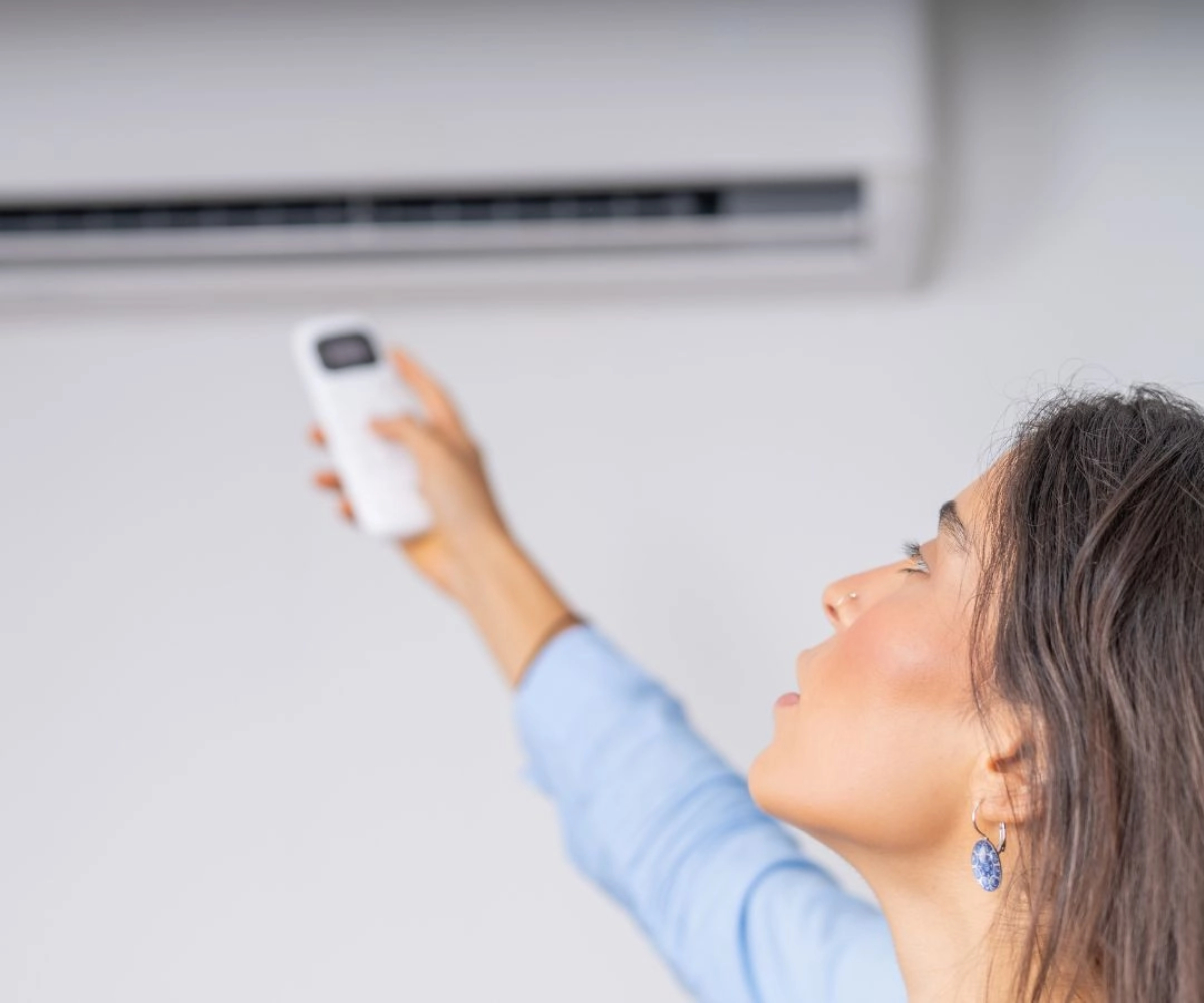 female pointing air con remote control at fixed unit on wall