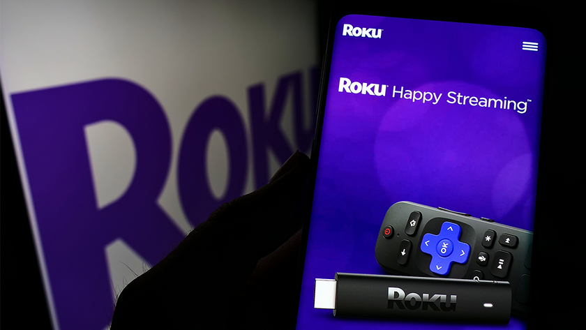 Person holding cellphone with website of American video streaming company Roku Inc. on screen in front of logo. Focus on center of phone display.