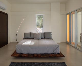 Brutalist bedroom with concrete floor, wood platform bed, wardrobes and patio doors