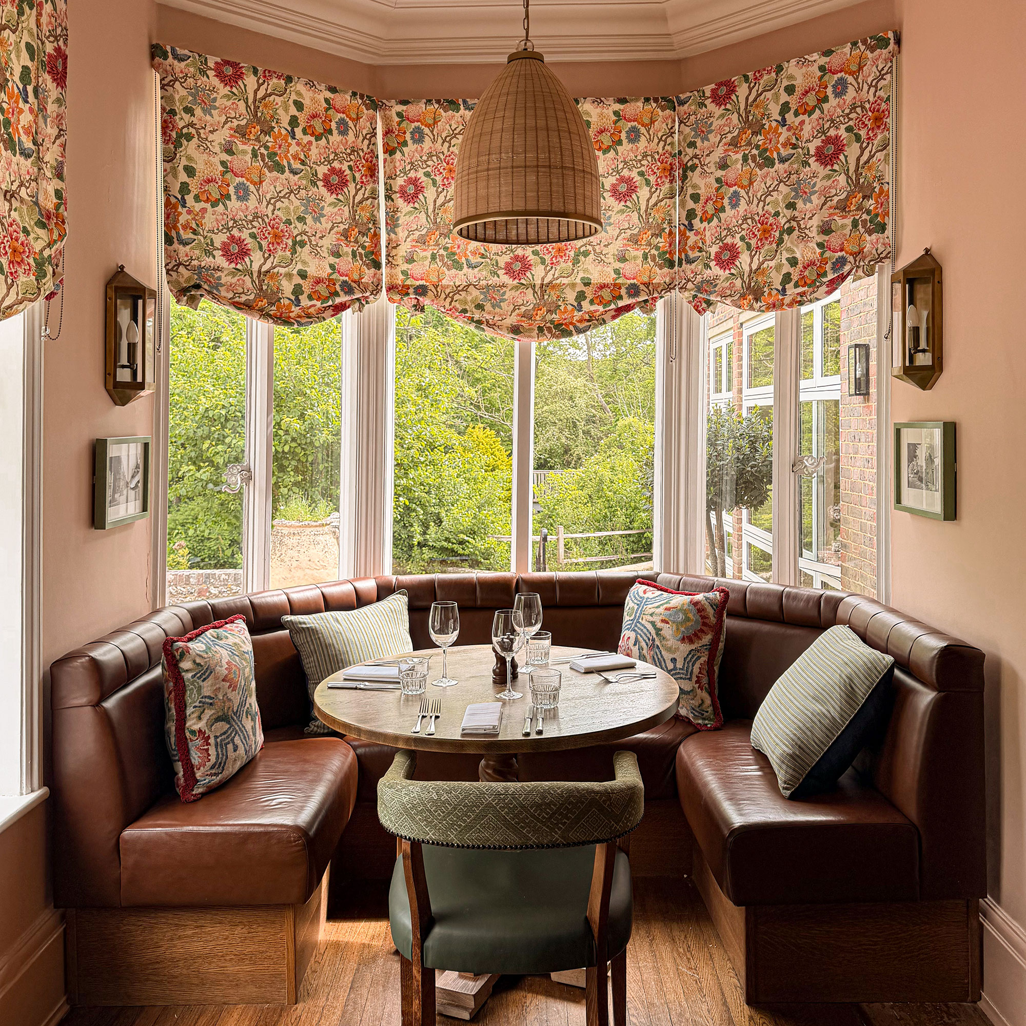 Dining nook in bay window area with U-shaped brown leather banquette and floral blinds