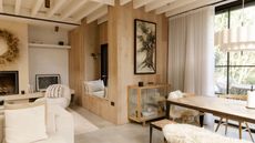 biophilic living room with timber walls, panelled ceiling, table with sheepskin draped over, glass cabinet, white sofas, and lots of natural light