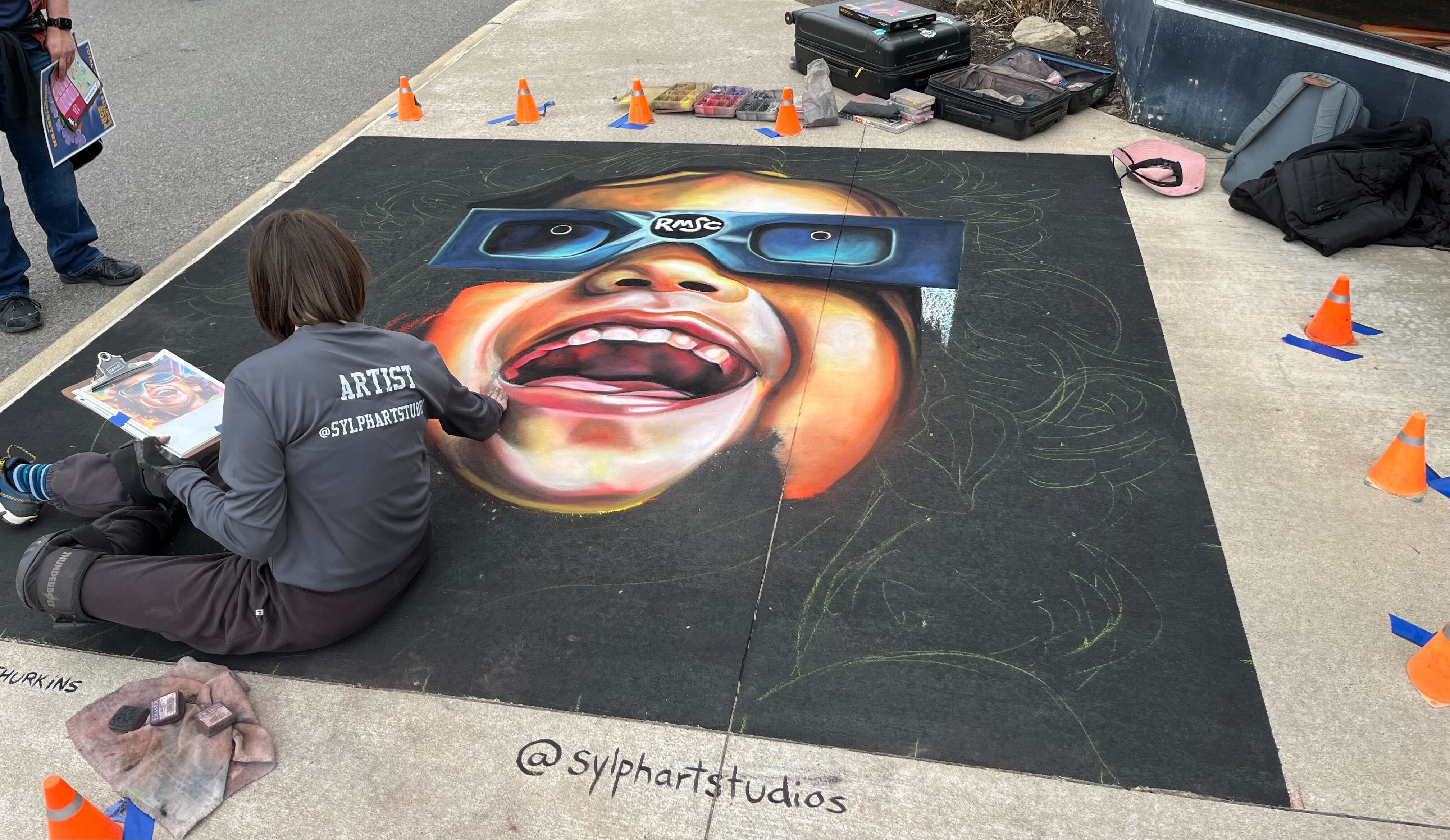 Chalk art with Erika Lalita Thurkins (Sylphartstudios) is capturing the joy of a solar eclipse in incredible detail outside the Eisenhart Planetarium at Rochester Museum and Science Center