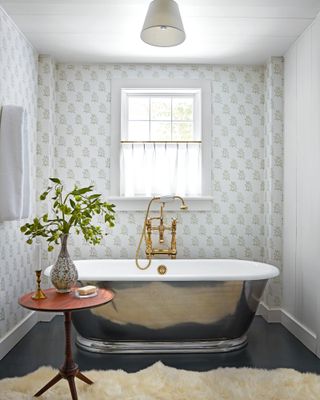 bathroom with silver tub, patterned wallpaper, sheepskin rug and wooden occasional table