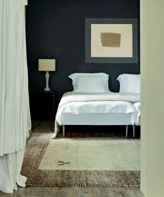 An example of black bedroom ideas showing a bedroom with cream curtains, a rug and bed linen