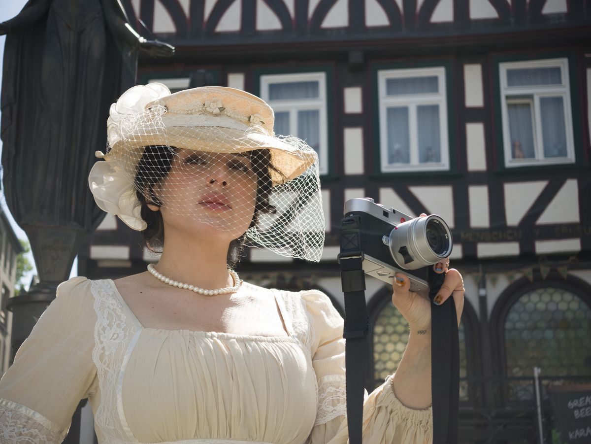 Insta360 Luna Ultra sample gallery: lady in period clothing holding a Leica camera, in quaint German town,