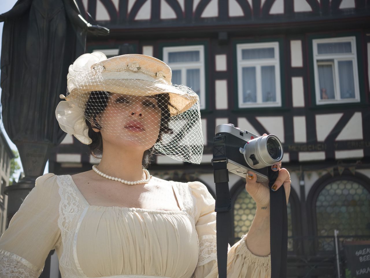 Insta360 Luna Ultra sample gallery: lady in period clothing holding a Leica camera, in quaint German town,