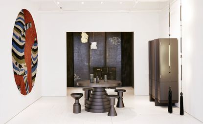 A dining area with a large round wall painting, a round layered dining table with round chairs and a large dark wood cupboard against the wall.