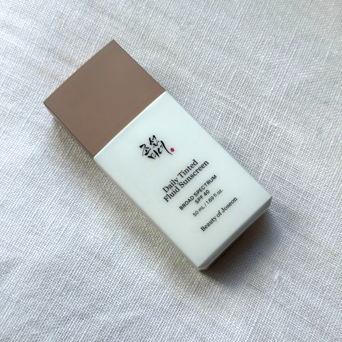 Bird's eye view of the Beauty of Joseon Daily Tinted Fluid Sunscreen laying on an off-white linen background 