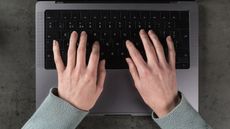 A woman types on a laptop keyboard, only her hands showing.