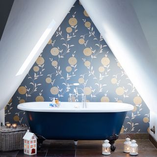 Blue freestanding bathtub in triangular shaped blue and white bathroom with blue gold and floral wallpaper