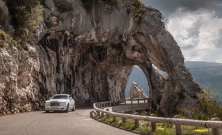 Rolls-Royce Phantom Series II driving on a road, with a rocky bridged opening carved in the mountain side