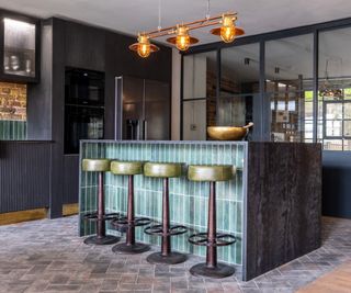 kitchen island diner unit in black marble with green glass brick tiles on one face and bar stools with green leather seats