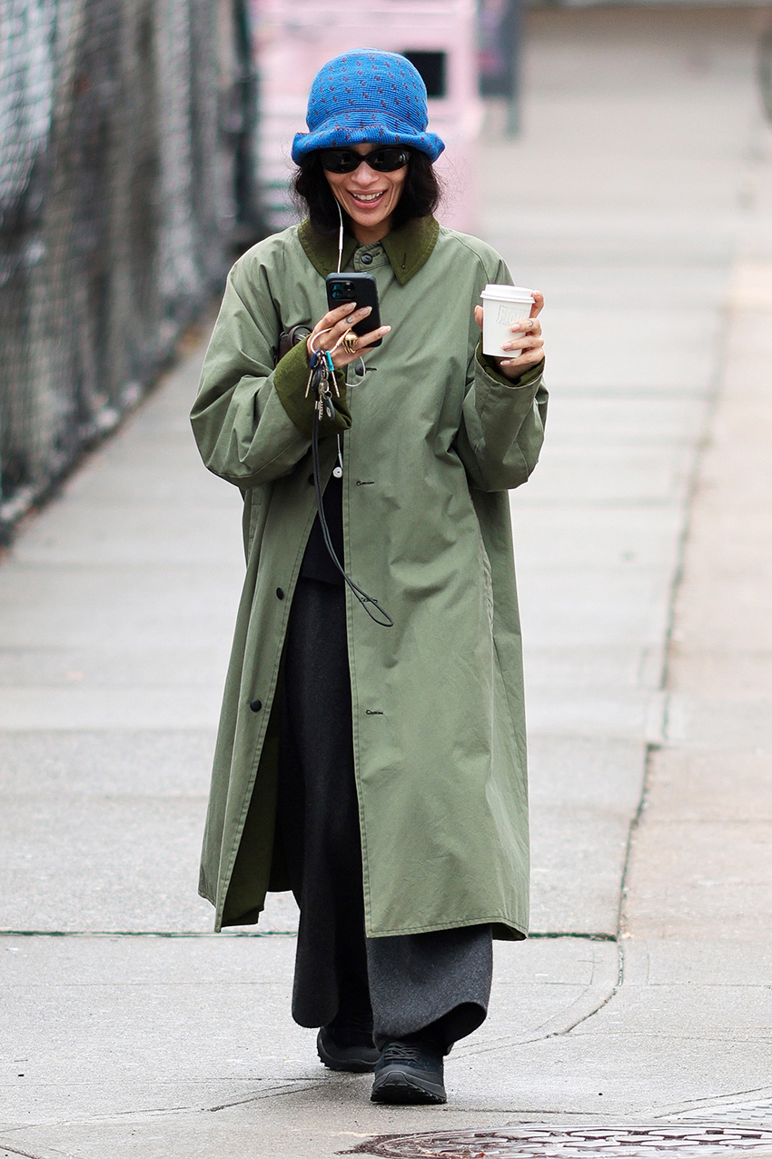 Zo&amp;euml; Kravitz walking with Harry Styles in NYC while wearing an olive green coat, black pants, black sneakers, a The Row Ingrid bag, and blue crochet bucket hat