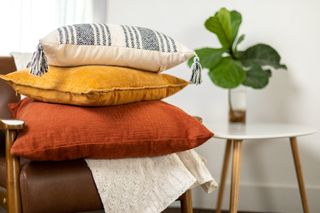 Three cushions on top of each other, one orange, one mustard, and one cream and blue striped.