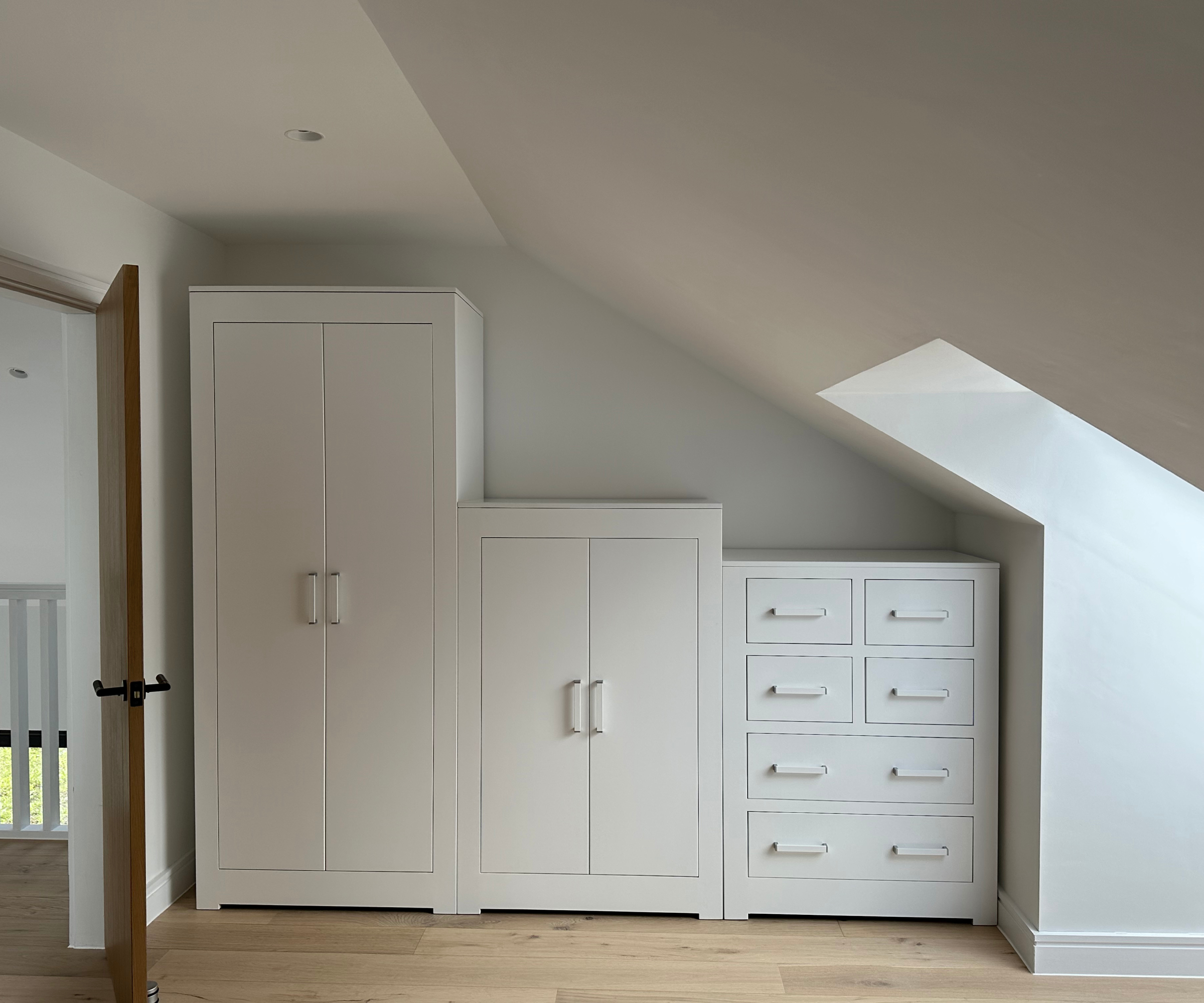 white bespoke freestanding wardrobes and drawer units below sloping ceiling in loft conversion bedroom