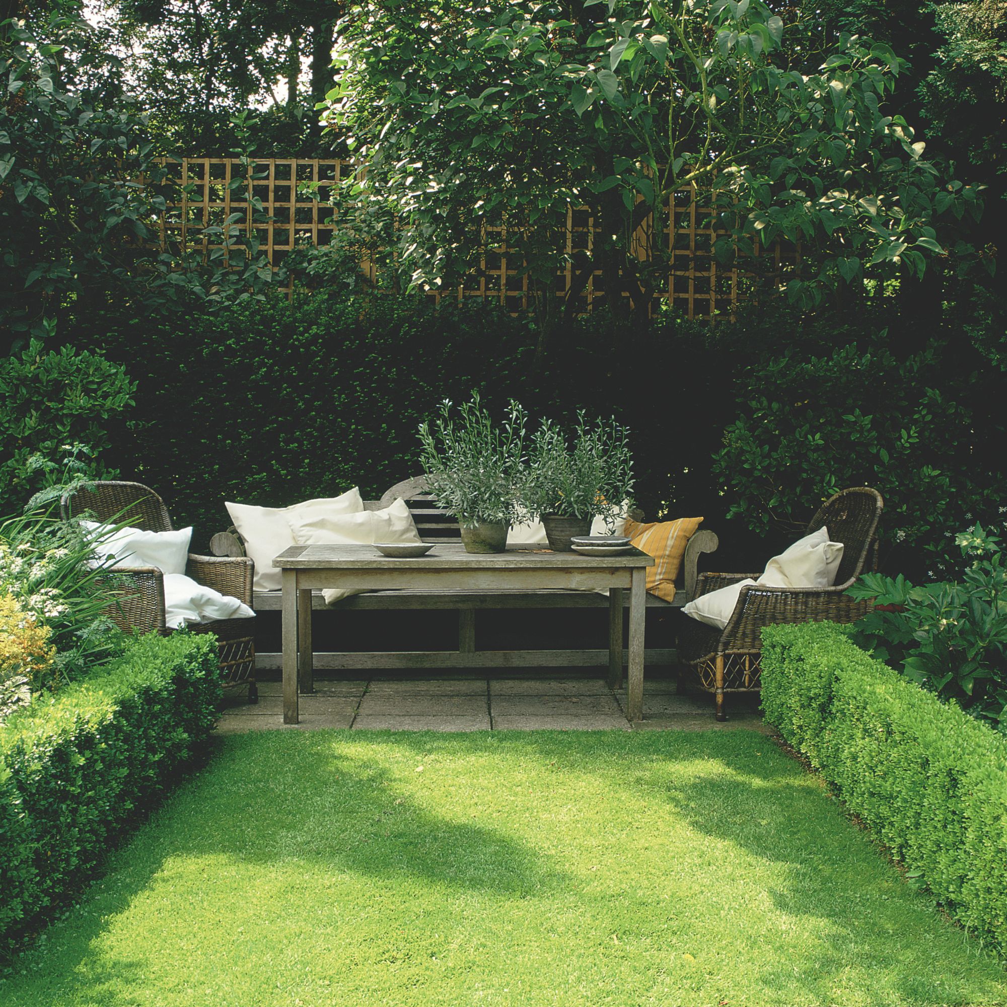 small garden laid to lawn with small hedges either side and a wooden furniture set at the end