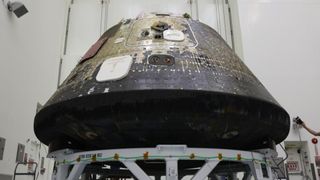 A space capsule with charred black on its bottom sits inside of a tall clean room. 