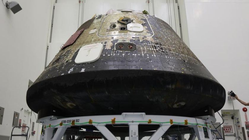 A space capsule with charred black on its bottom sits inside of a tall clean room. 