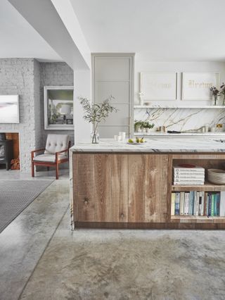 A white, rustic kitchen design with polished concrete flooring, a kitchen island designed in wood with white marble countertops, and pale gray cabinetry.