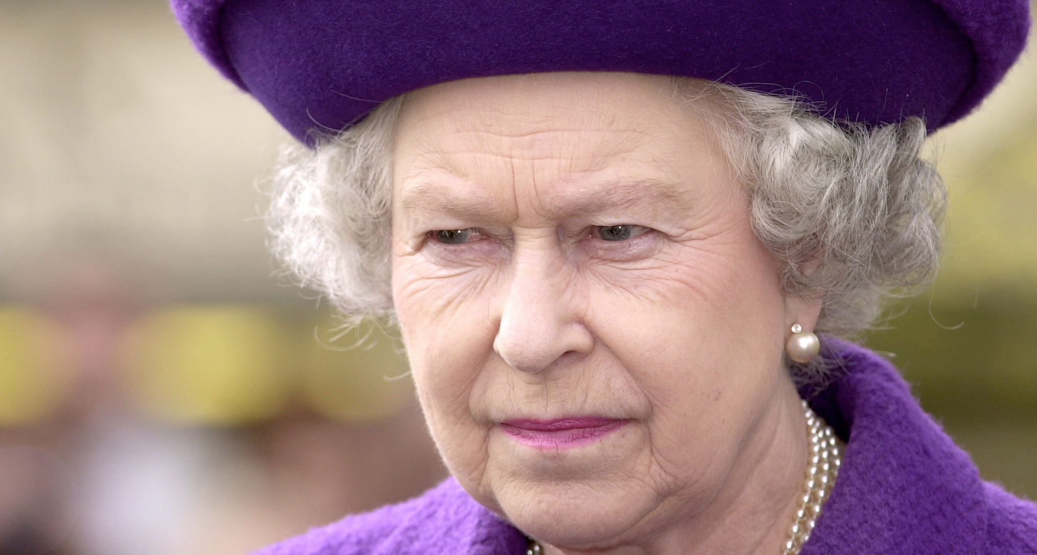 Queen Elizabeth wearing a purple hat and coat and scowling