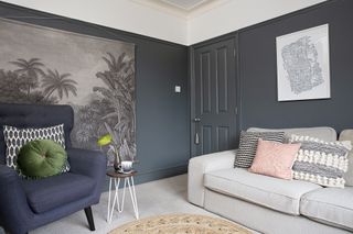 Living room with dark navy painted walls and contrasting grey carpet, a grey sofa with blush pink cushions, and a blue armchair