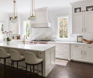 All white kitchen with mahogany hardwood flooring, a large kitchen island with white bar chairs and low pendant lighting