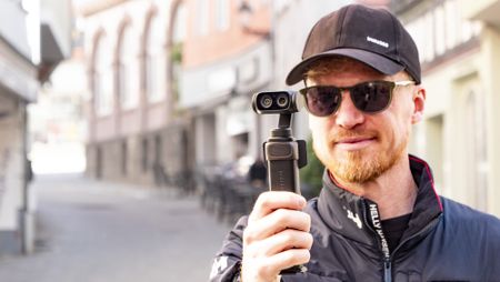 Man holding the Insta360 Luna Ultra vlogging camera on a sunny day in a old town